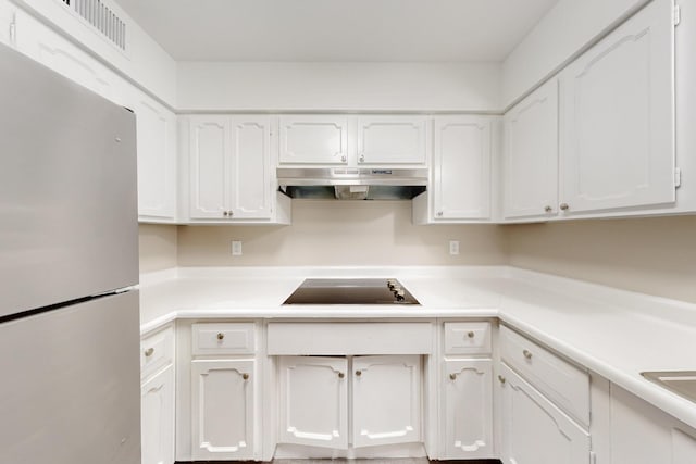 kitchen featuring under cabinet range hood, freestanding refrigerator, white cabinets, light countertops, and black electric cooktop