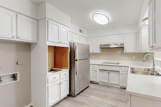 kitchen featuring under cabinet range hood, a sink, white cabinets, and freestanding refrigerator