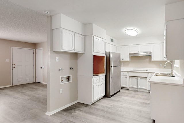 kitchen featuring freestanding refrigerator, a sink, electric stovetop, under cabinet range hood, and white cabinetry