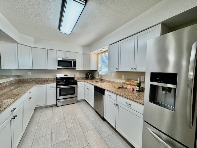 kitchen with light stone countertops, appliances with stainless steel finishes, a textured ceiling, white cabinetry, and a sink