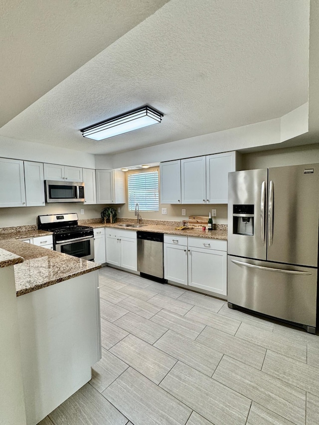 kitchen featuring a sink, white cabinets, light stone countertops, and stainless steel appliances