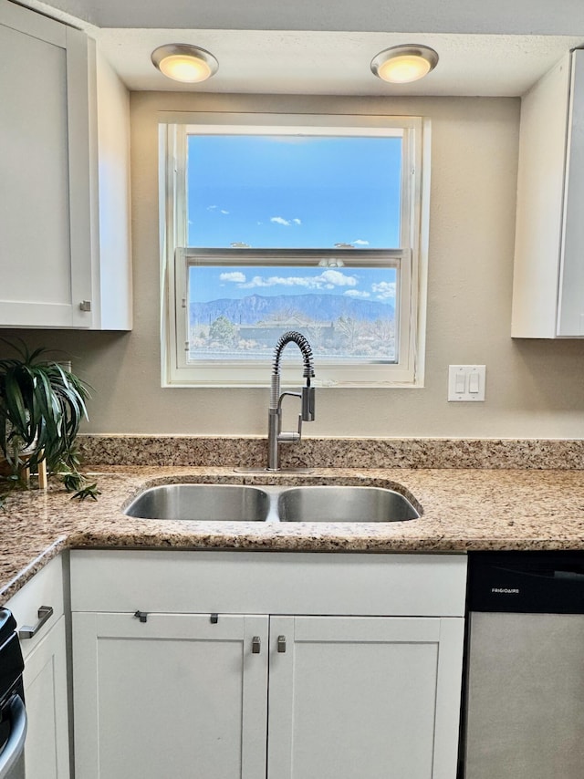 kitchen with dishwasher, white cabinets, light stone countertops, and a sink