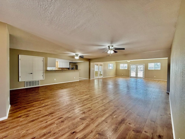 unfurnished living room with visible vents, baseboards, ceiling fan, hardwood / wood-style flooring, and a textured ceiling