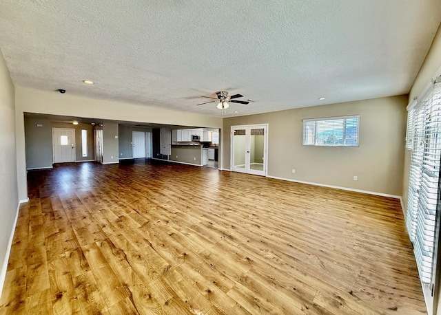 unfurnished living room with a textured ceiling, baseboards, light wood-type flooring, and a ceiling fan