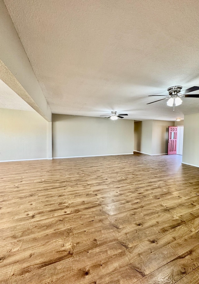 empty room with a ceiling fan, wood finished floors, baseboards, and a textured ceiling