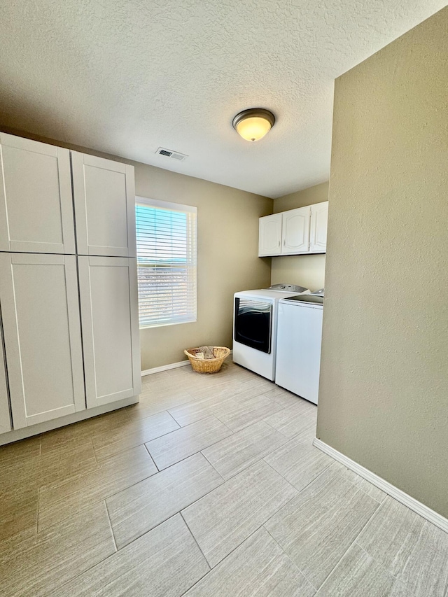 clothes washing area with washing machine and clothes dryer, visible vents, baseboards, a textured wall, and cabinet space