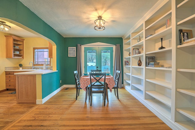 dining area featuring a textured ceiling, light wood-style floors, arched walkways, and baseboards