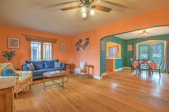 living area featuring wood finished floors, arched walkways, and ceiling fan