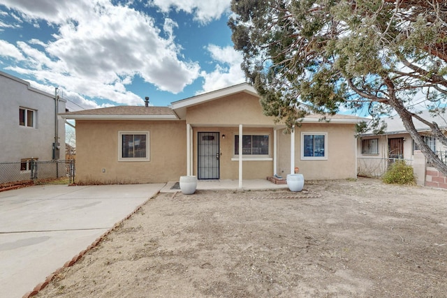 view of front of house featuring covered porch, stucco siding, and fence