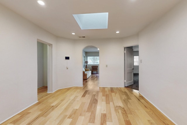 hallway featuring a skylight, visible vents, arched walkways, and light wood-type flooring