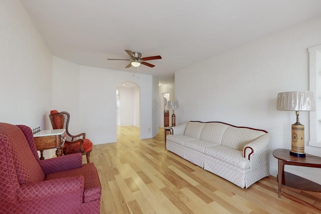 living room with arched walkways, wood finished floors, and a ceiling fan