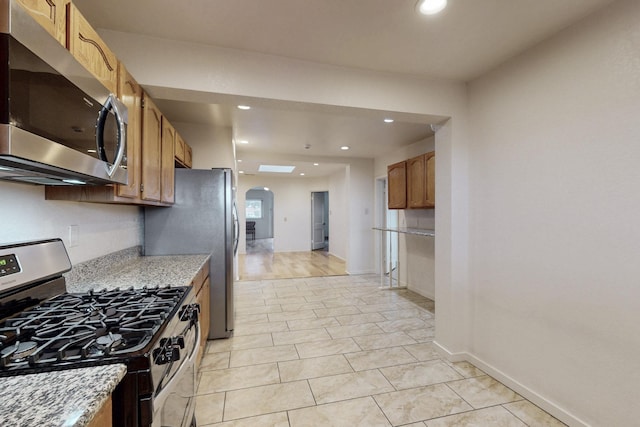 kitchen with arched walkways, recessed lighting, stainless steel appliances, and brown cabinets