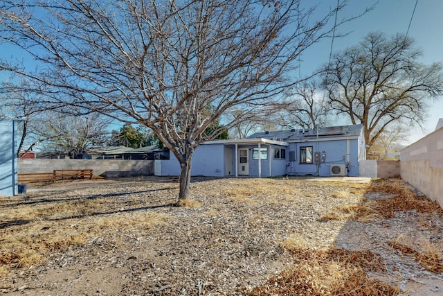 rear view of house featuring stucco siding, roof mounted solar panels, and fence