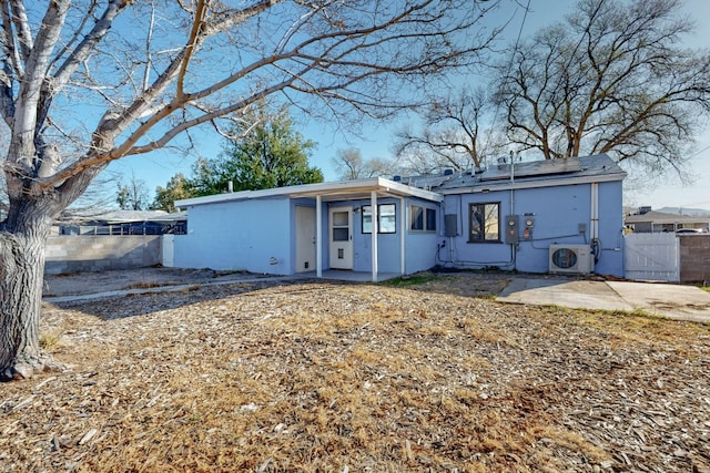 view of front facade with ac unit, stucco siding, roof mounted solar panels, fence, and a patio area