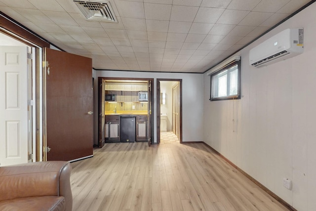 unfurnished living room featuring visible vents, a wall mounted air conditioner, light wood-type flooring, and baseboards