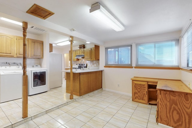 kitchen featuring visible vents, under cabinet range hood, washer and dryer, a peninsula, and light tile patterned floors