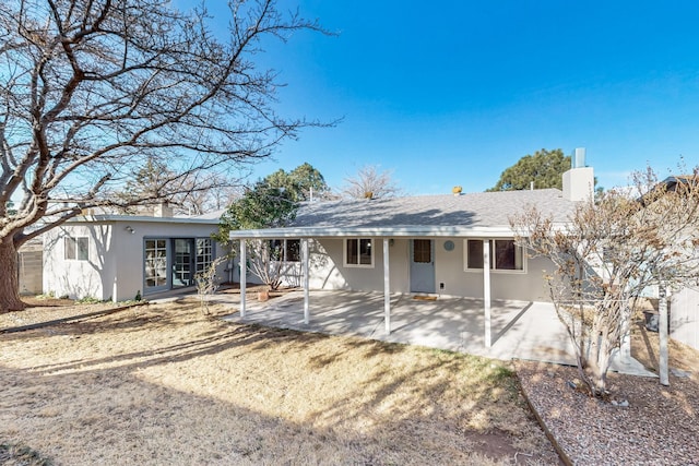 rear view of house featuring stucco siding, a chimney, and a patio area