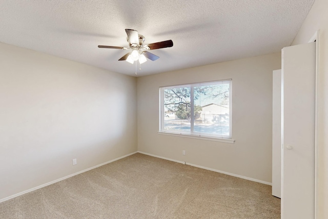 spare room with a textured ceiling, light colored carpet, baseboards, and ceiling fan