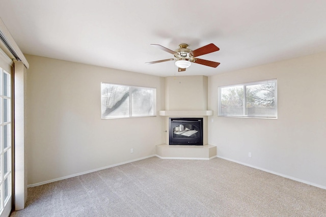 unfurnished living room with a glass covered fireplace, carpet, baseboards, and a ceiling fan