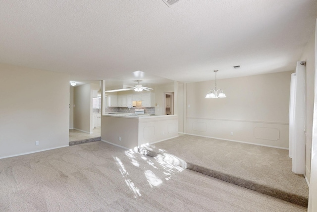 unfurnished living room featuring ceiling fan with notable chandelier, light colored carpet, and a textured ceiling