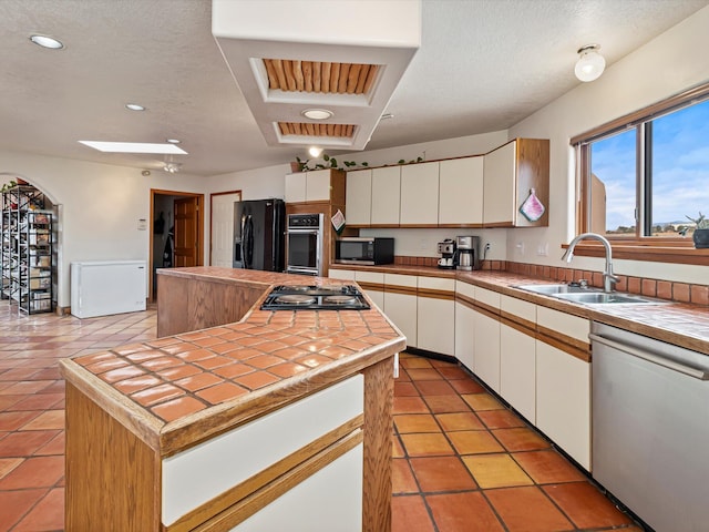 kitchen with a kitchen island, tile countertops, white cabinets, black appliances, and a sink