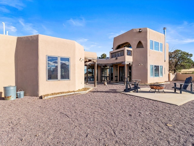 rear view of property with stucco siding, a patio, and a fire pit