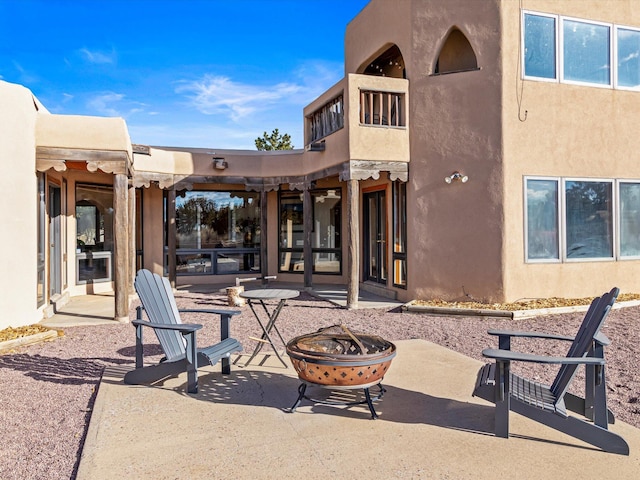 back of house with a balcony, stucco siding, an outdoor fire pit, and a patio