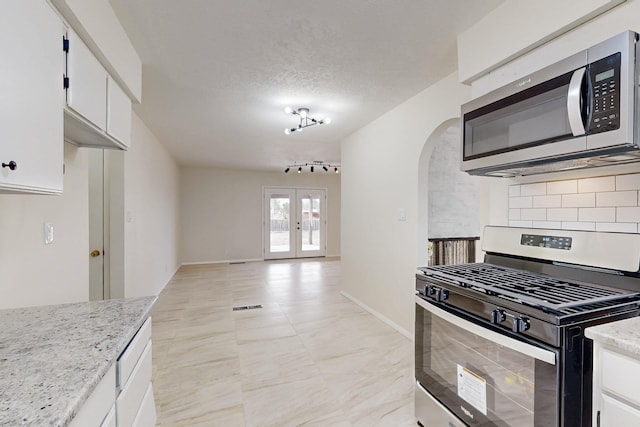 kitchen featuring arched walkways, white cabinetry, stainless steel appliances, and tasteful backsplash