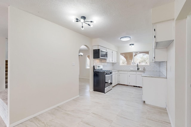 kitchen featuring arched walkways, stainless steel appliances, light countertops, white cabinetry, and backsplash