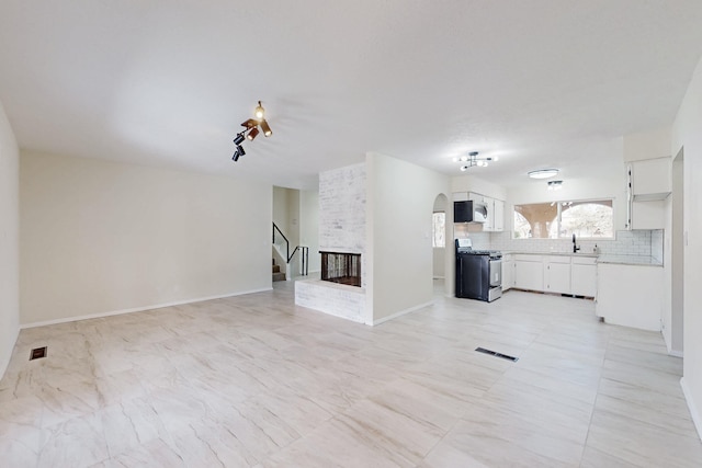 unfurnished living room featuring stairway, visible vents, baseboards, arched walkways, and a sink