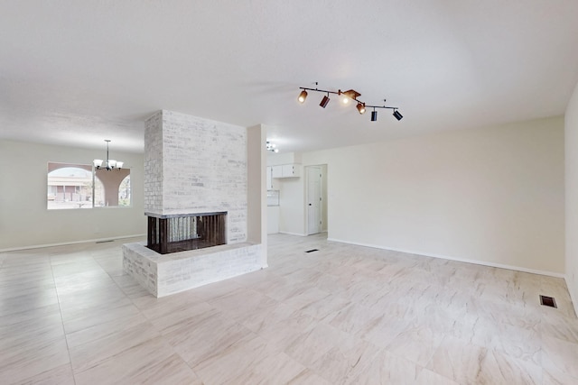 unfurnished living room featuring visible vents, baseboards, a notable chandelier, and a brick fireplace