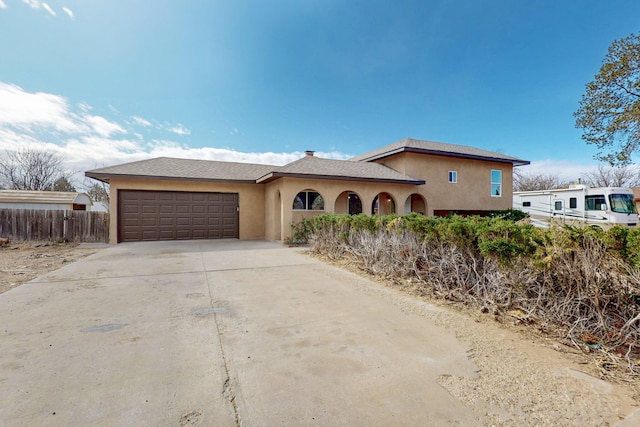 view of front of house with stucco siding, driveway, an attached garage, and fence