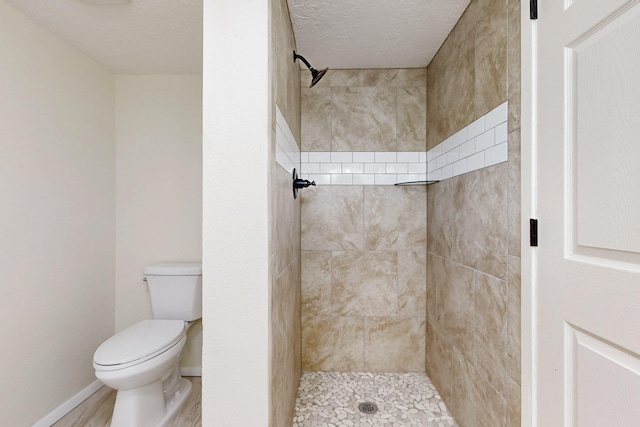 bathroom featuring a tile shower, a textured ceiling, toilet, and baseboards