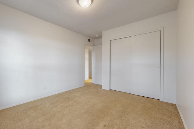 unfurnished bedroom featuring light colored carpet, visible vents, a closet, and baseboards