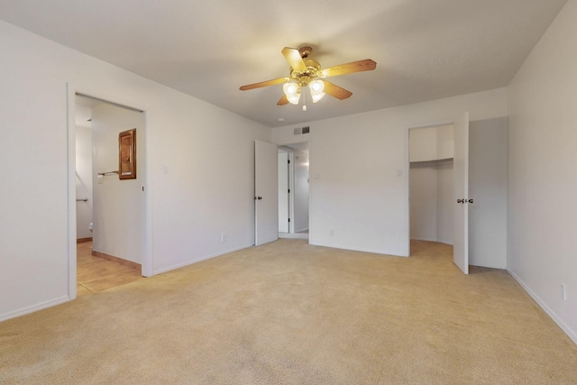 unfurnished bedroom with visible vents, a walk in closet, ceiling fan, light carpet, and ensuite bath