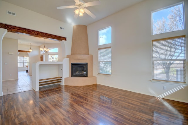 unfurnished living room with plenty of natural light, ceiling fan with notable chandelier, visible vents, and wood finished floors