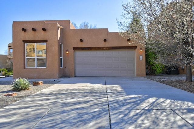 pueblo revival-style home with stucco siding, concrete driveway, and an attached garage