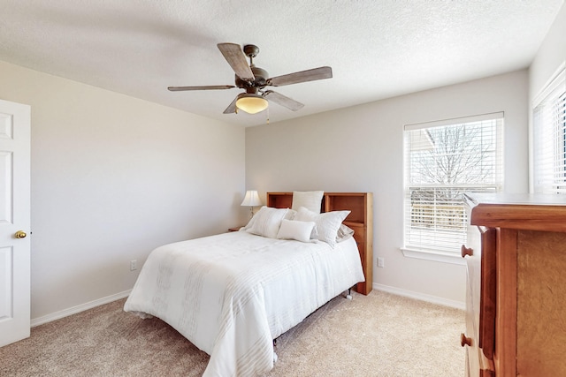 bedroom with baseboards, light carpet, a textured ceiling, and a ceiling fan