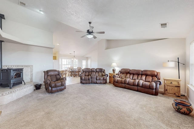 carpeted living area with visible vents, lofted ceiling, a wood stove, and ceiling fan with notable chandelier