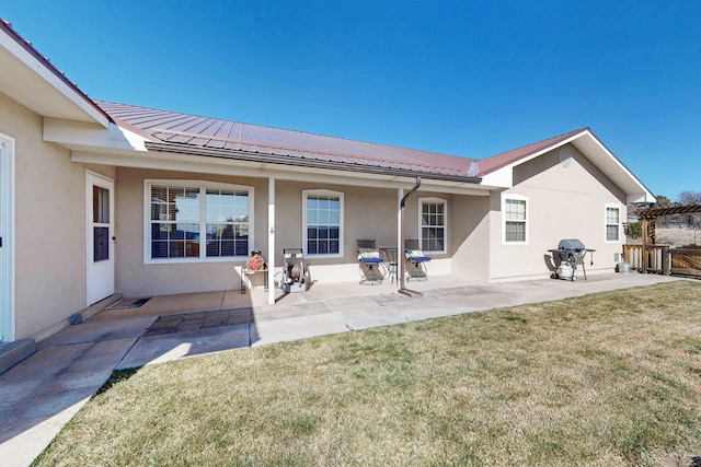 rear view of house with stucco siding, a yard, metal roof, and a patio area