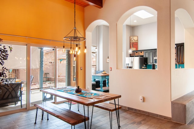 dining space with wood finished floors, baseboards, beam ceiling, arched walkways, and a notable chandelier