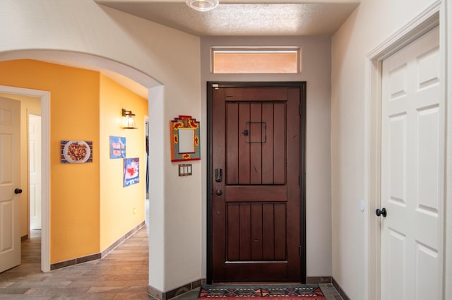 foyer with light wood-type flooring, arched walkways, a textured ceiling, and baseboards