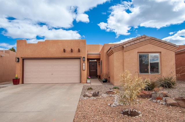 pueblo revival-style home with a garage, driveway, and stucco siding