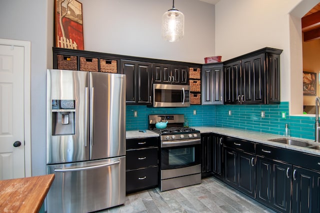 kitchen featuring decorative backsplash, stainless steel appliances, dark cabinetry, and a sink