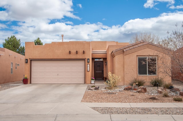 pueblo-style house featuring stucco siding, driveway, and an attached garage