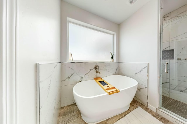 full bath with a freestanding tub, a marble finish shower, and tile walls