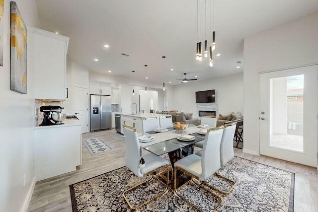 dining space with visible vents, recessed lighting, light wood-style flooring, a glass covered fireplace, and a ceiling fan