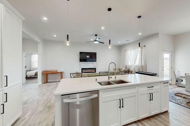 kitchen featuring a sink, stainless steel dishwasher, open floor plan, a fireplace, and light wood finished floors