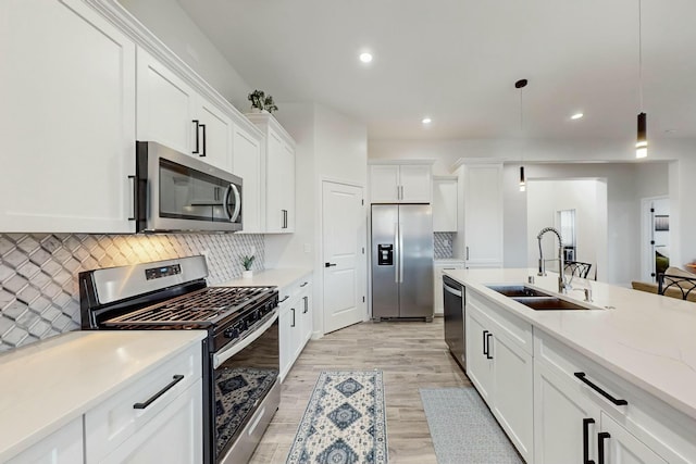 kitchen featuring a sink, stainless steel appliances, white cabinets, light wood-style floors, and decorative light fixtures