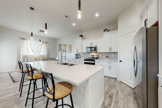 kitchen featuring a center island with sink, a sink, appliances with stainless steel finishes, a kitchen bar, and tasteful backsplash